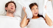 Snoring? Trouble Sleeping? Try Exercise. Picture of a caucasian male sleeping in bed and a caucasian female in bed with her pillow pulled over her ears.