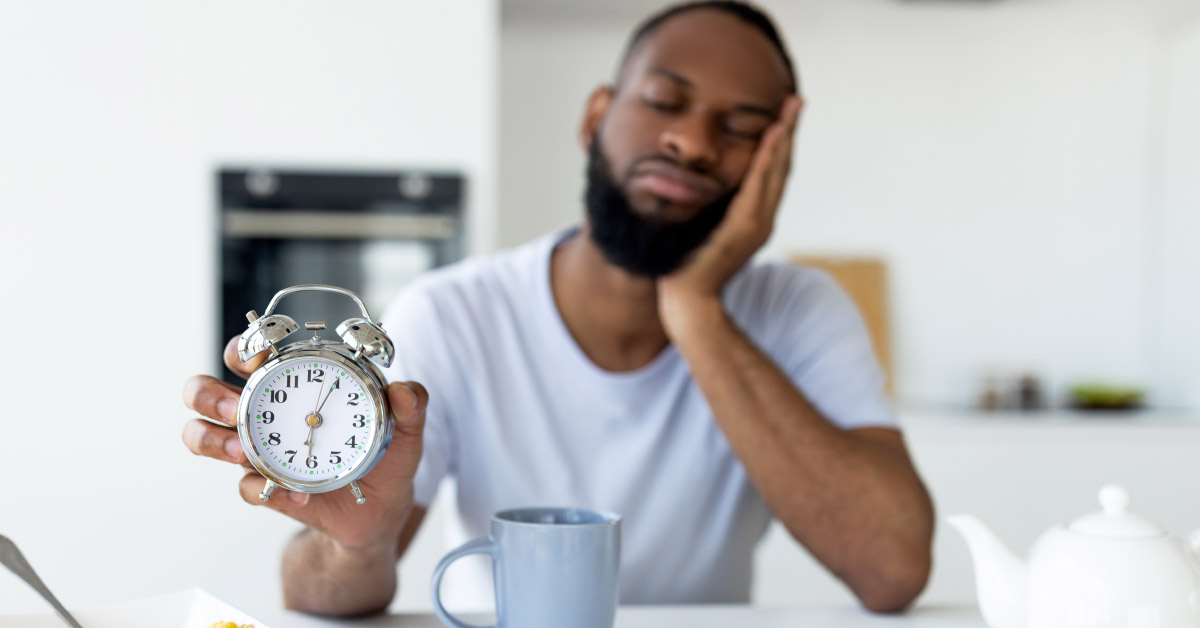 Sleepy African American man with an alarm clock and a cup of coffee.